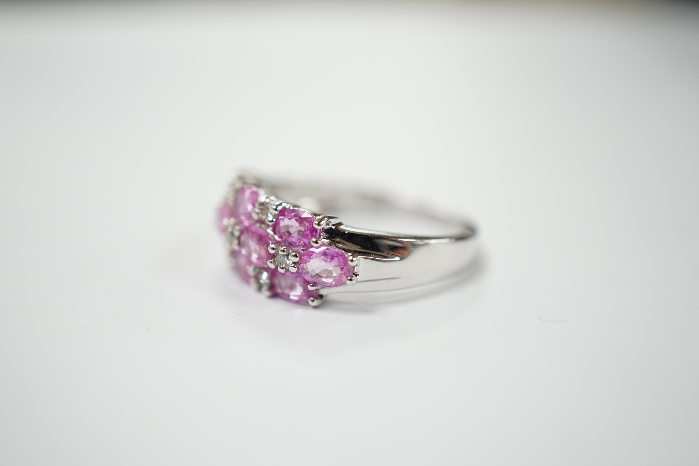 A modern 14k white metal, pink sapphire and diamond cluster set half hoop ring (two sapphires loose), size O, gross weight 4.7 grams.